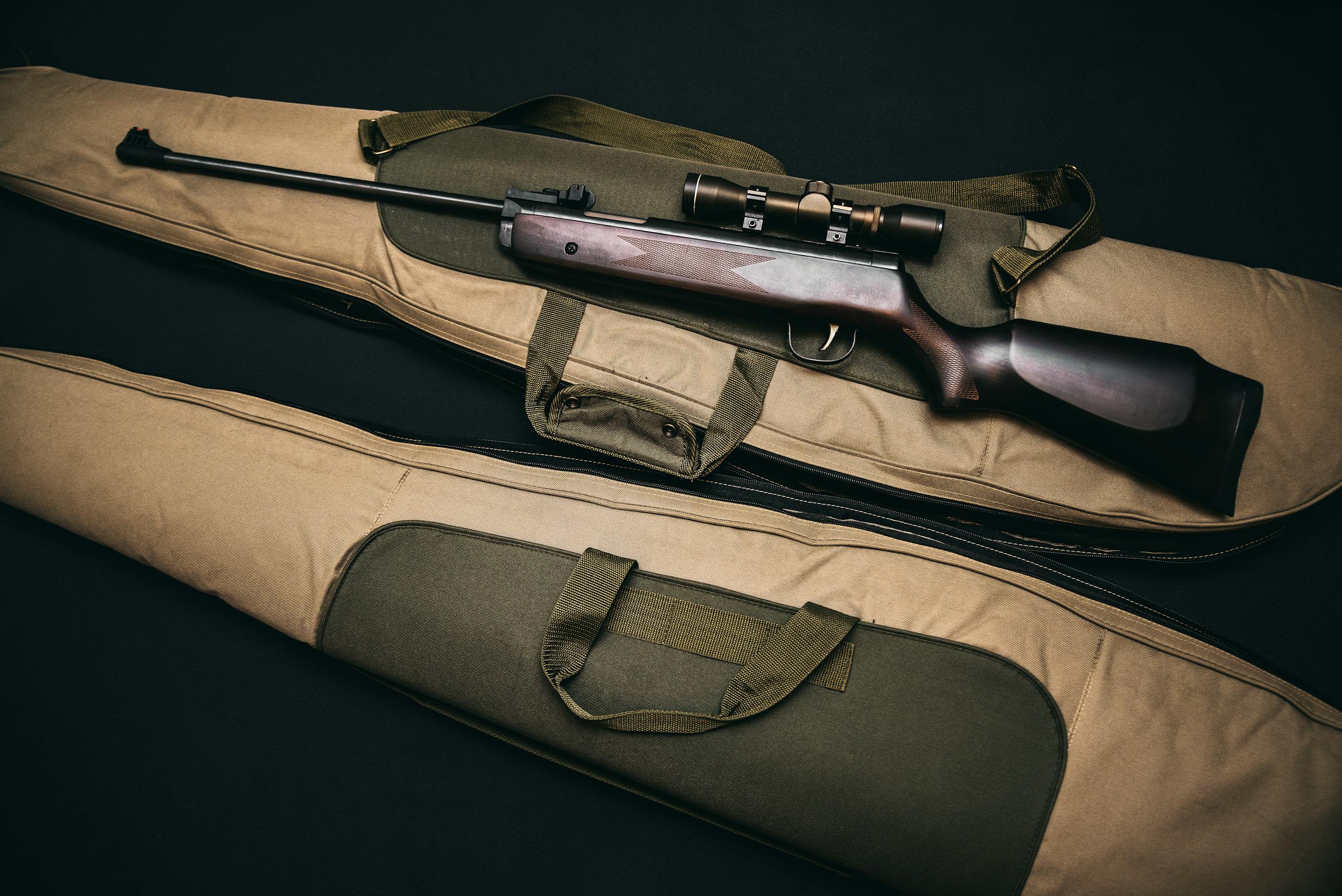Close-up of a hunting rifle with a scope on a carrying bag, showcasing firearms and hunting gear.